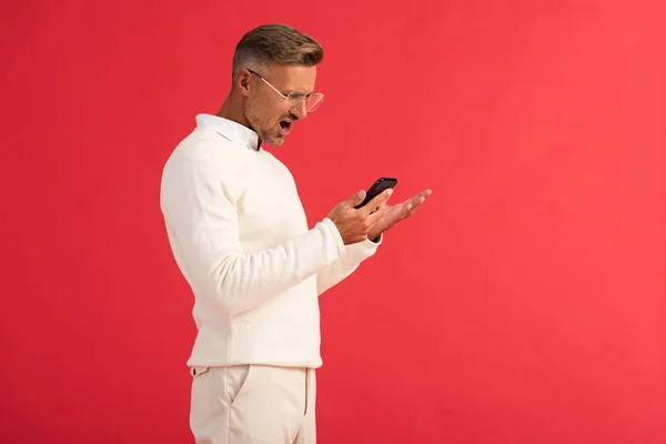 Verrast Man Bril Kijken Naar Smartphone Gebaren Geïsoleerd Rood — Stockfoto