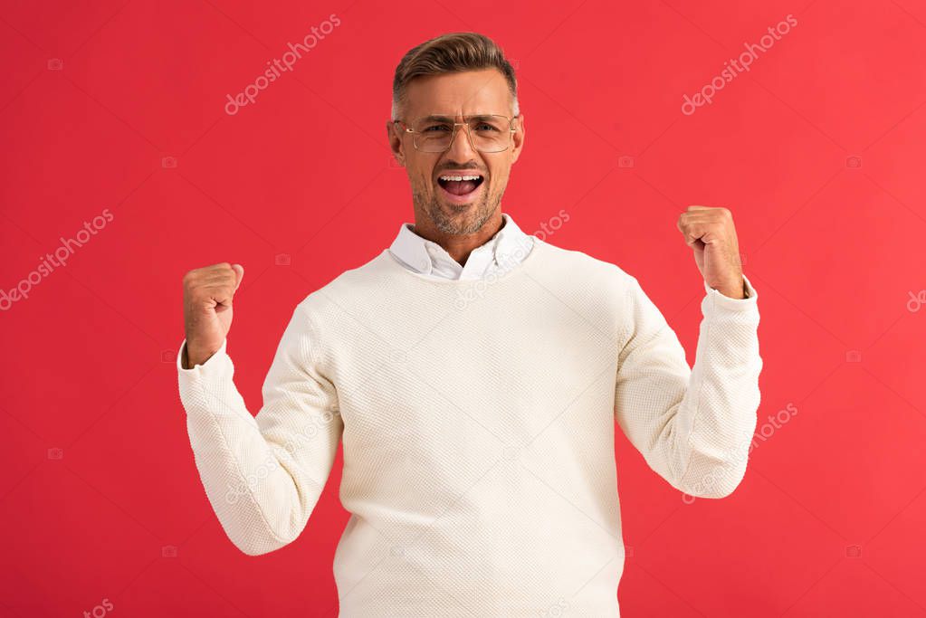 excited man in glasses celebrating triumph isolated on red 