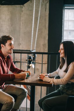 Kahve dükkanının balkonunda birbirine bakan gülümseyen çift.
