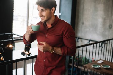 Gülümseyen adam kahve dükkanında kapuçinoyla balkonda duruyor.