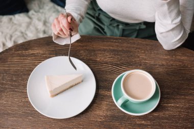 Cheesecake yiyen ve kafede kahve içen bir kadın.