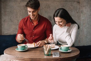 Peynirli kek yiyen ve kahve dükkanında cappuccino içen mutlu çift.