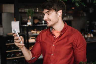 Kablosuz kulaklıklı gülen adam akıllı telefon kullanıyor.