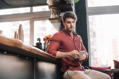 Yakışıklı adam, akıllı telefon kullanarak, kablosuz kulaklıklarla barın yanında oturuyor.