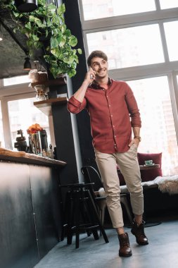 smiling handsome man walking near bar counter and talking on smartphone