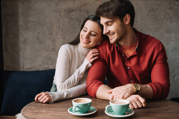 smiling romantic young couple hugging and drinking coffee in coffee shop