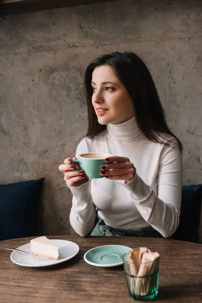 Uśmiechnięta Kobieta Pije Kawę Odwraca Wzrok Sernika Kawiarni — Zdjęcie stockowe