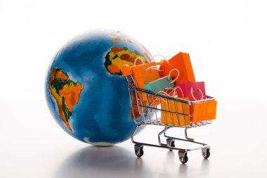 Beyaz, e-ticaret kavramı üzerine dünya yakınında alışveriş torbaları olan oyuncak alışveriş arabası.