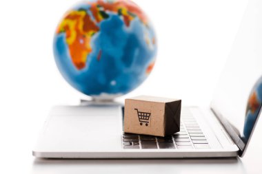 Dünya yakınındaki dizüstü bilgisayardaki oyuncak kutusunun seçici odak noktası beyaz, e-ticaret konseptinde izole edilmiş.