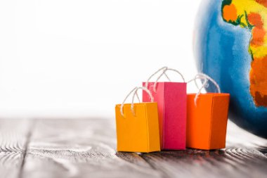 Dünyanın yakınındaki masada beyaz, e-ticaret konseptine izole edilmiş renkli oyuncak alışveriş çantaları.