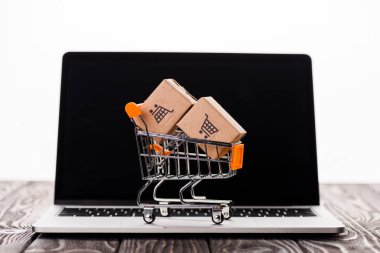 toy shopping cart with small carton boxes on laptop with blank screen isolated on white, e-commerce concept clipart