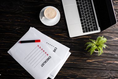 Liste yakınındaki dizüstü bilgisayarın üst görüntüsü, bitki, kırmızı keçeli kalem ve masa üzerindeki kahve fincanı, e-ticaret konsepti