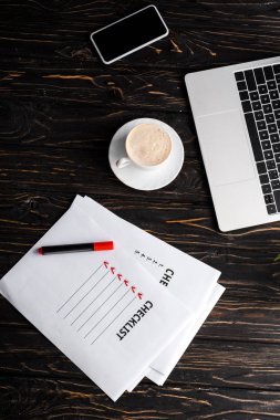 Kontrol listesi olan kağıtların yanındaki aletlerin üst görüntüsü, kırmızı keçeli kalem ve masa üzerinde bir fincan kahve, e-ticaret konsepti