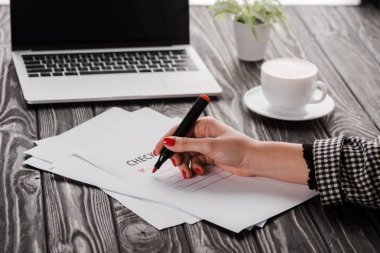 İşkadını, kontrol listesi, fincan ve dizüstü bilgisayarın yanında kalem tutarken çekilmiş görüntüsü, e-ticaret konsepti