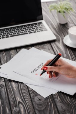 İşkadını kırmızı kalemle kontrol listesi, bardak ve dizüstü bilgisayarın yanında e-ticaret konseptini tutuyor.