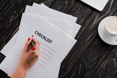 İşkadını, kontrol listesinin yanında işaret kalemi ve masanın üzerinde bir fincan kahve tutuyor. 