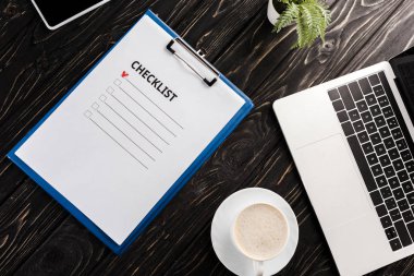 Bilgisayarın yanında kontrol listesi harfleri olan panonun üst görüntüsü, masa üzerinde bitki ve fincan kahve, e-ticaret konsepti