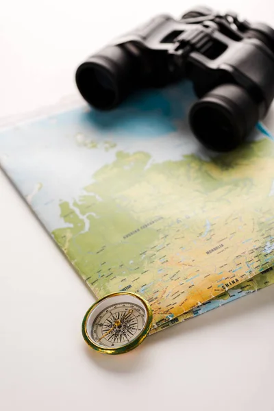 golden compass near map and binoculars on white