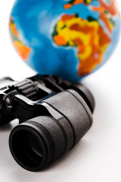 selective focus of black binoculars near globe on white 
