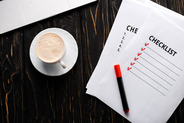 top view of papers with checklist and red marker pen near cup of coffee on table 