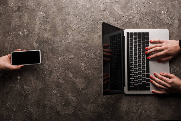 top view of businesswoman holding smartphone with blank screen near colleague typing laptop, e-commerce concept