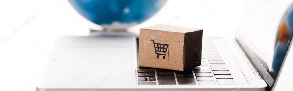 panoramic shot of toy box on laptop keyboard near globe isolated on white, e-commerce concept