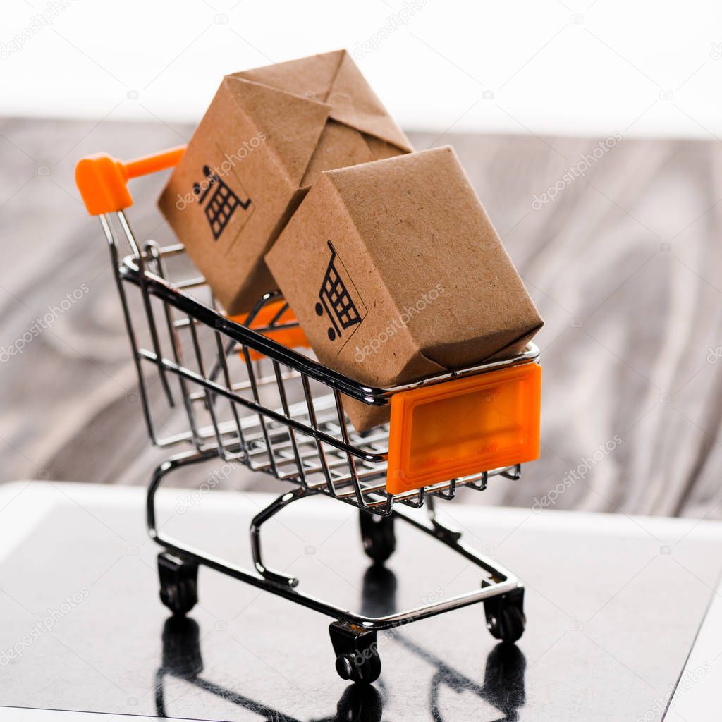 close up of toy shopping cart with small boxes on digital tablet, e-commerce concept