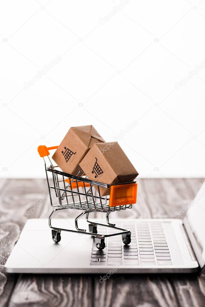 selective focus of toy shopping cart with small boxes on laptop isolated on white, e-commerce concept