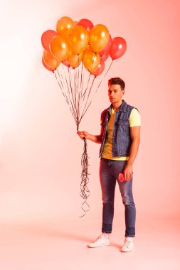 Yakışıklı adam pembe üzerinde turuncu balonlar tutuyor. 