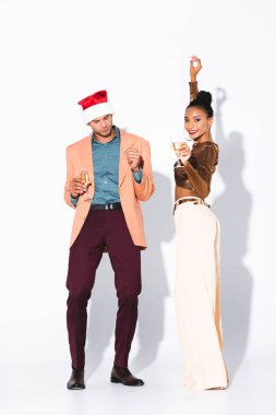 Güzel Afrikalı Amerikalı kız elinde şampanya bardağıyla Noel Baba şapkalı adamın yanındaki kameraya bakıyor. 