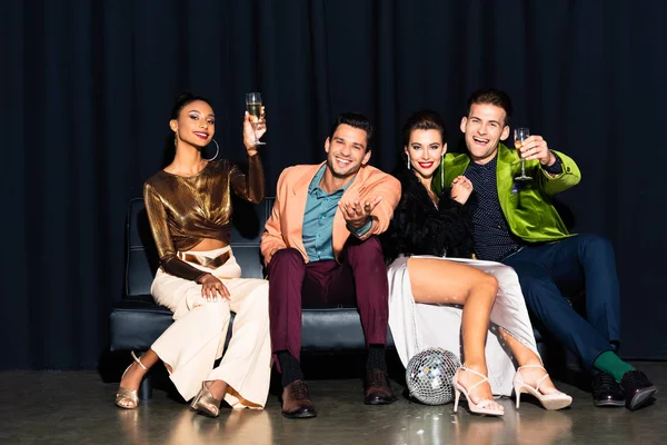 Cheerful Multicultural Women Handsome Men Holding Champagne Glasses While Sitting — Stock Photo, Image