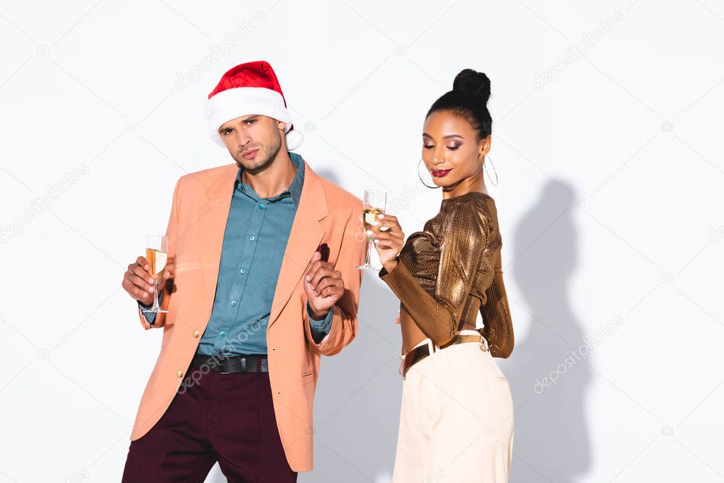 beautiful african american girl holding champagne glass near man in santa hat on white 