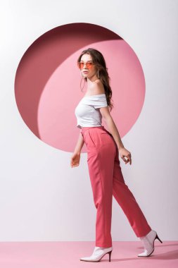 Güneş gözlüklü güzel kız, beyaz ve pembe üzerinde yürüyor. 