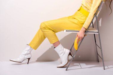 Sandalyede oturan ve beyaz üzerinde sarı muz tutan bir kadın. 
