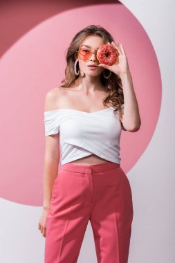 Güzel kız yüzünü lezzetli çöreklerle kaplıyor ve pembe ve beyaz üzerinde duruyor. 