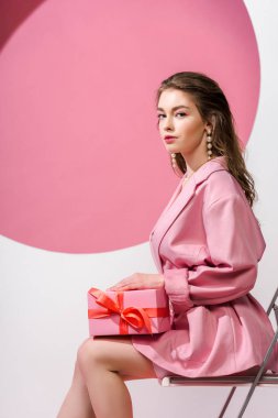 Beyaz ve pembe üzerinde otururken hediye kutusunu tutan çekici kız. 