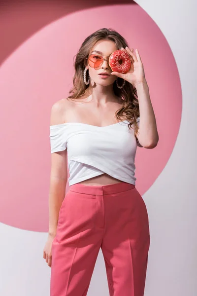 美丽的女孩用美味的甜甜圈盖住脸 站在粉色和白色的上面 — 图库照片