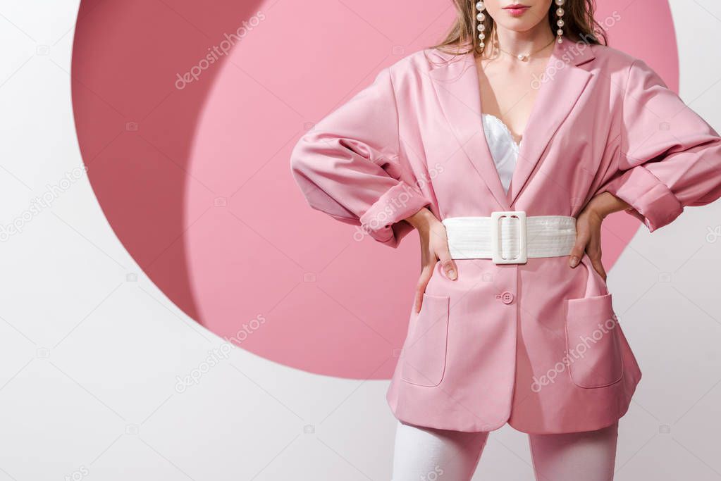 cropped view of stylish woman standing with hands on hips on white and pink 