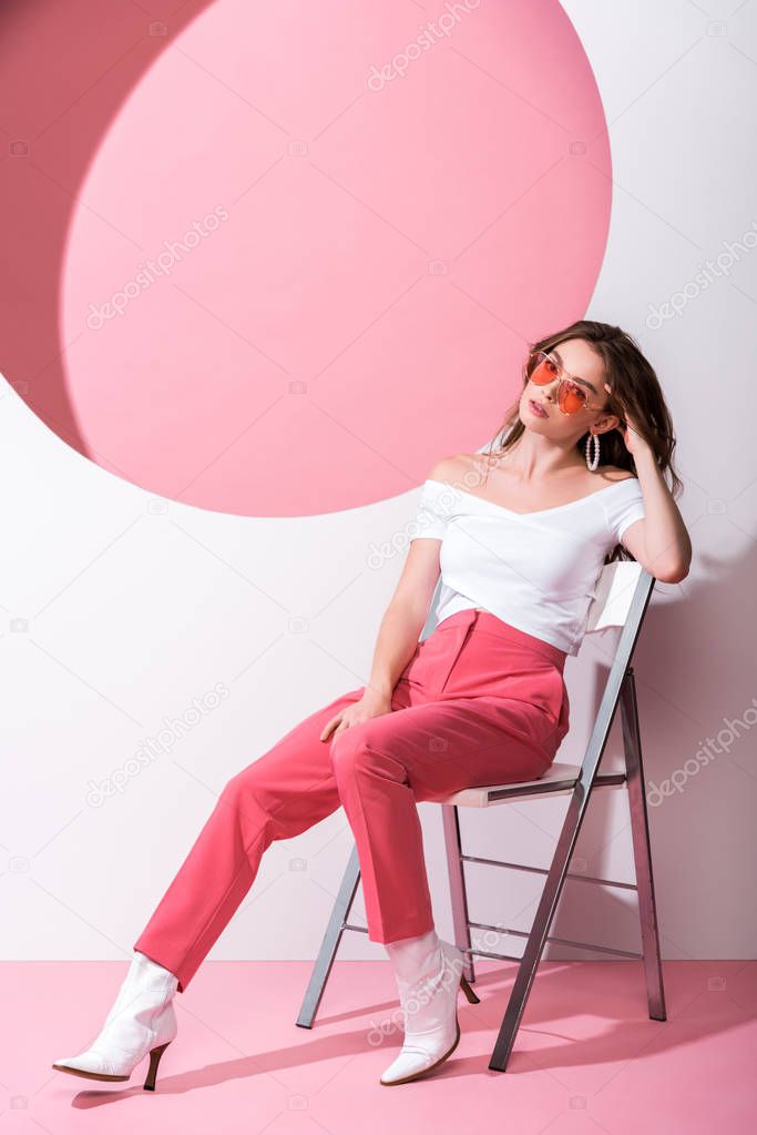 stylish woman sitting on chair on pink and white 