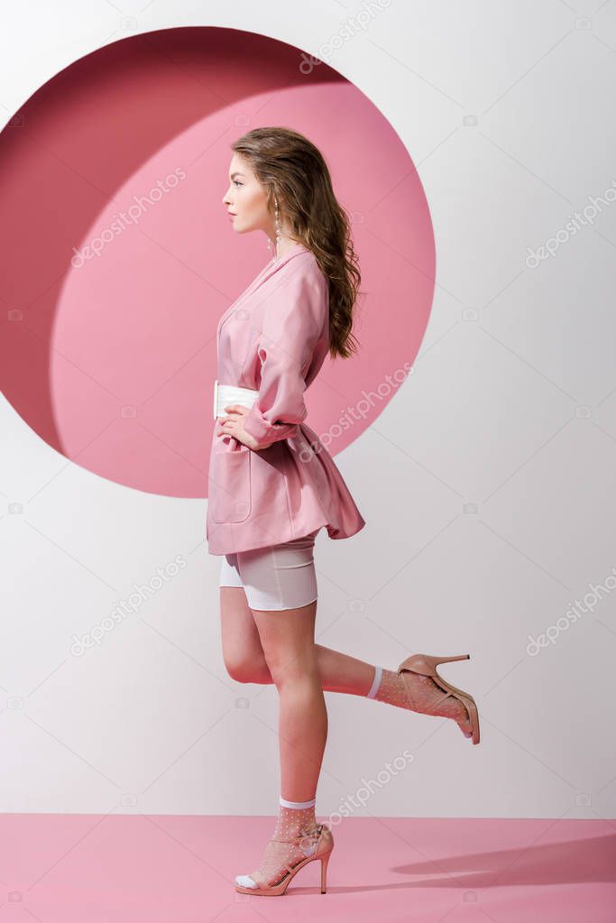 side view of woman standing with hand on hip on pink and white 