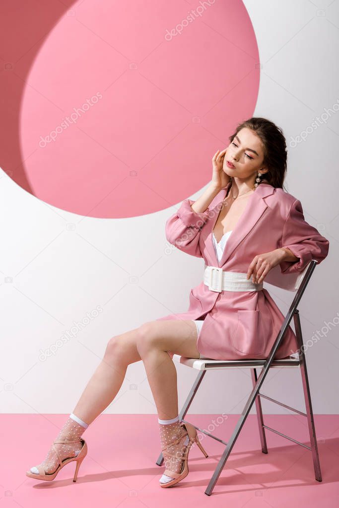 stylish woman in blazer with belt sitting on chair on white and pink 