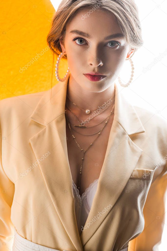 beautiful young woman in necklace and earrings looking at camera on orange and white 