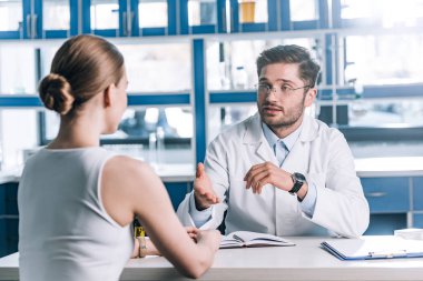 Gözlüklü yakışıklı doktorun seçici odağı hastaya bakıyor ve klinikte el kol hareketi yapıyor. 