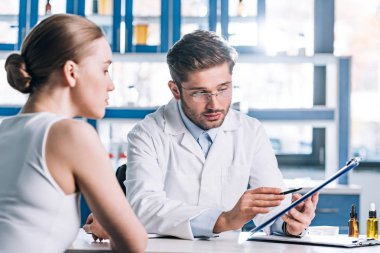 selective focus of allergist holding clipboard near patient in clinic  clipart