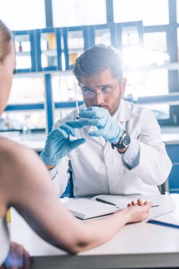 Plastik eldivenli alerji uzmanının seçici odağı klinikte kadının yanında şırınga tutuyor. 