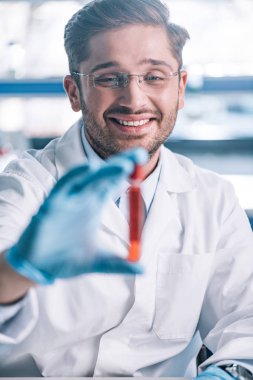 Kırmızı sıvı ile test tüpü tutan mutlu bağışıklık bilimcilerin seçici odağı 