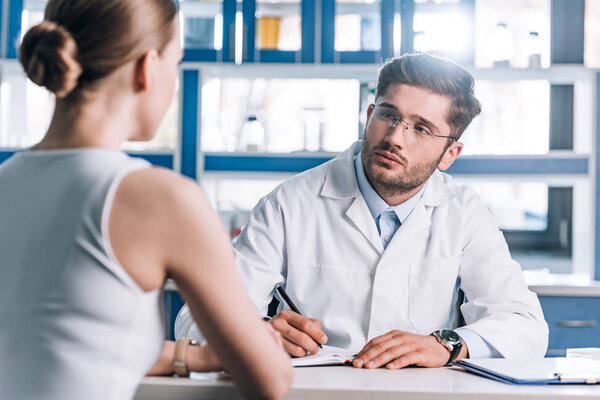 selective focus of handsome doctor holding pen and looking at patient 