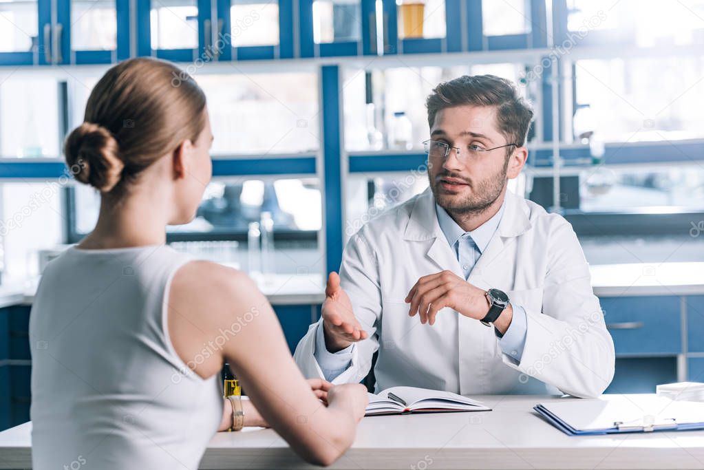 selective focus of handsome doctor in glasses looking at patient and gesturing in clinic 