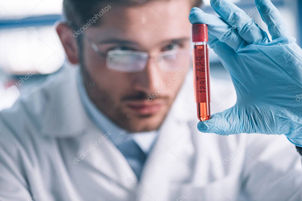 selective focus of bearded immunologist holding test tube with red liquid 