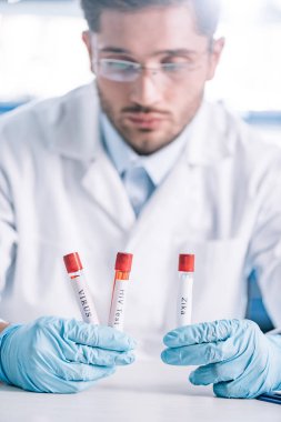 Gözlüklü sakallı immünolojistin seçici odağı elinde harflerle test tüpleri tutuyor. 